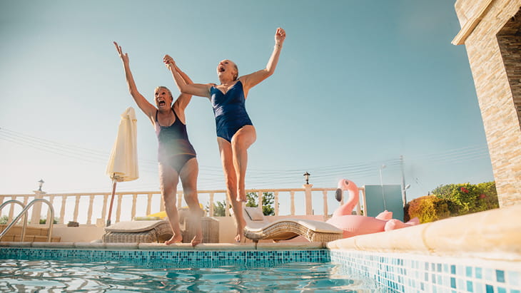 Two senior women jumping into a swimming pool